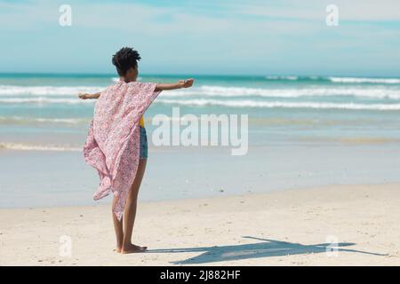 Carefree african american young woman with short hair stretching arms at beach against sky in summer Stock Photo