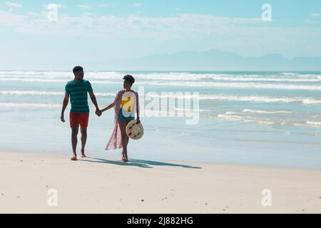 African american young woman with short hair holding boyfriend's hands while walking at beach Stock Photo
