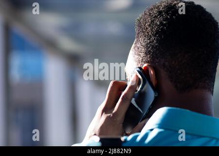 Rear view of african american businessman talking on smartphone in corridor at workplace Stock Photo