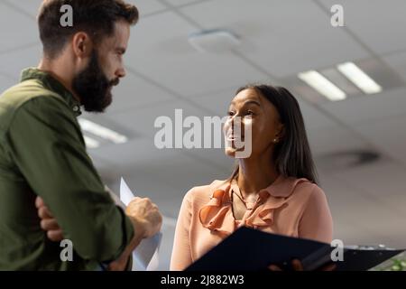 Happy biracial businesswoman discussing over document with caucasian businessman in workplace Stock Photo