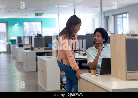 Confident biracial male and female colleagues discussing together in cubicle at modern workplace Stock Photo