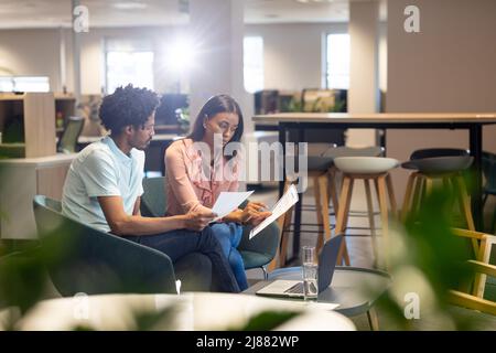 Confident female and male biracial colleagues discussing over document at modern workplace Stock Photo