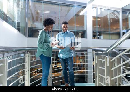 Smiling african american male and female professionals discussing over file on staircase Stock Photo