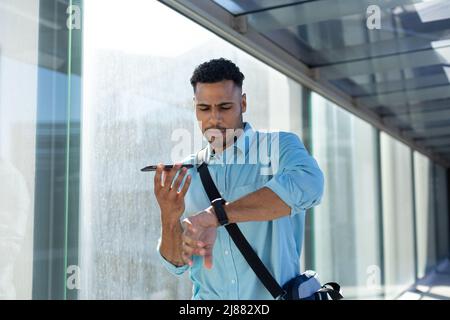 African american businessman checking time while talking on smartphone through speaker in corridor Stock Photo