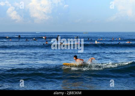 Many surfers riding waves in the sea at Batu Bolong Beach in Canggu, Bali, Indonesia with blue ocean and blue sky on a sunny day. Stock Photo