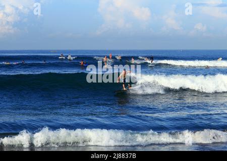 Many surfers riding waves in the sea at Batu Bolong Beach in Canggu, Bali, Indonesia with blue ocean and blue sky on a sunny day. Stock Photo