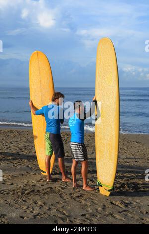 Two male Caucasian surfers standing at Batu Bolong Beach in Canggu, Bali, Indonesia carrying their long boards or malibu surfboards. Stock Photo