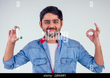 Young indian man in a denim jeans jacket using asthma inhaler at studio white background Stock Photo