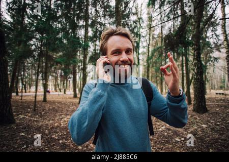 Young adult man talking on the phone standing over white brick wall stressed with hand on head, shocked with shame and surprise face, angry and frustr Stock Photo