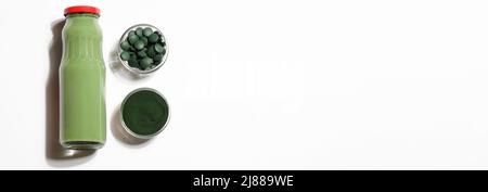 green smoothie in bottle and spirulina algae powder and pills in glass bowl on white background.useful habits,self care and healthy concept. banner Stock Photo