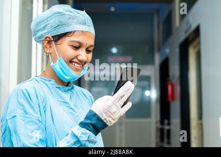 Happy smiling medical practitioner busy using mobile phone at hospital corridor - concept of using social medica, technology and internet Stock Photo