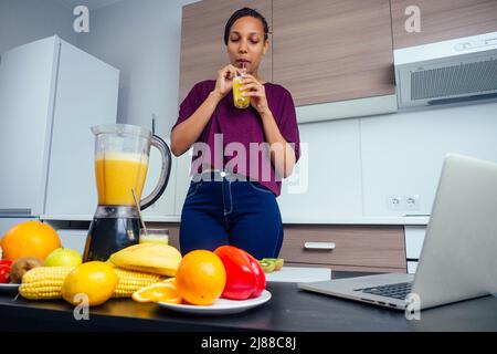 latino woman working at juice bar and cutting fruits, making fresh smoothies mixer blender from bananas,orange and melon. she useing eco metal Stock Photo