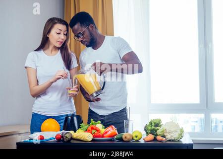 african american man with asian woman making smoothie at home, useing eco tubes from metall Stock Photo