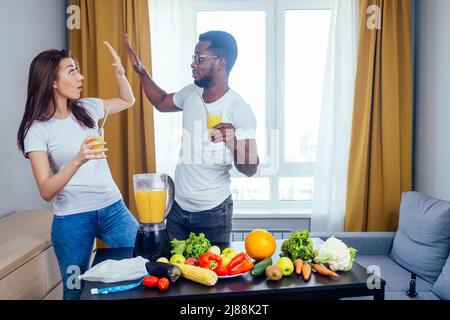 african american man with asian woman making smoothie at home, useing eco tubes from metall high five Stock Photo