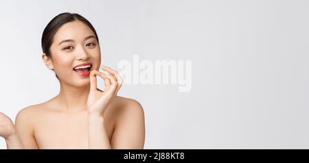 Young attractive asian woman who takes a capsule or pill. Isolated over white background. Stock Photo