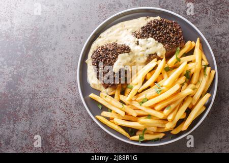 Classic French dish steak au poivre is a filet mignon with a crunchy peppercorn crust and rich Cognac sauce served with french fries close-up in a pla Stock Photo