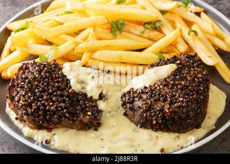 Classic French dish steak au poivre is a filet mignon with a crunchy peppercorn crust and rich Cognac sauce served with french fries close-up in a pla Stock Photo