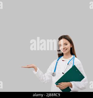 Brunette female general practitioner with patient's medical record standing and showing on empty space for your ad text. medical advertising Stock Photo