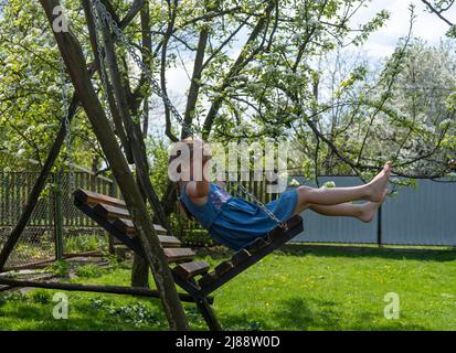 little girl barefoot rides on a swing on a sunny day Stock Photo