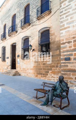 Bronze statue of the poet Antonio Machado seated on a bench in front of the façade of a medieval palace in the Spanish town of Baeza. Stock Photo