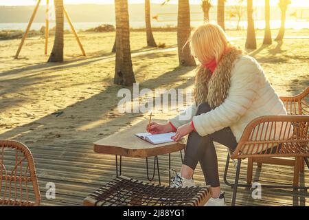 A middle-aged woman with blonde hair sits in a street cafe.  Stock Photo