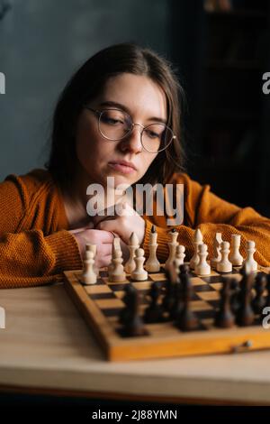 Pensive woman sitting at table in living room while thinking about next  chess move. Stock Photo by DC_Studio