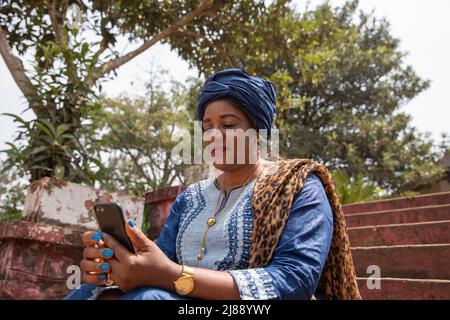 African woman dressed traditionally uses her smartphone, woman and technology concept Stock Photo