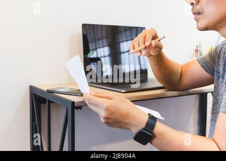 Man reading document paper while working on laptop at home. Stock Photo