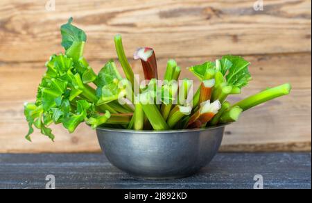 Young juicy rhubarb stalks on a wooden table in a metal bowl. Fresh juicy vegetarian organic food. Stock Photo