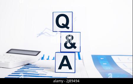 Answers to financial questions. Cubes with qa abbreviation, calculator and charts. FAQ in business, statistics and economic areas. High quality photo Stock Photo