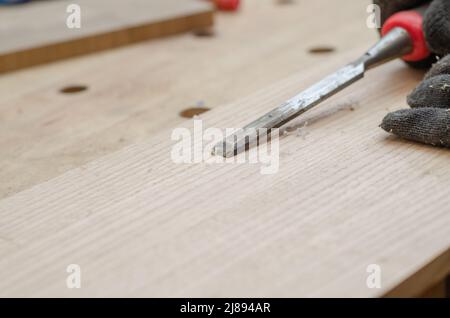 Woodworker using chisel cuts slot on wooden board close up Stock Photo