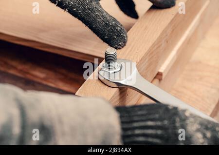 Male hands tighten nut on thread of bolt screwed into wooden structure. Stock Photo