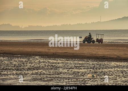 Scene of morning sunrise with silhouette of man riding an ATV on the beach off Pantai Beserah Beach near Kuantan in Pahang, Malaysia. Stock Photo