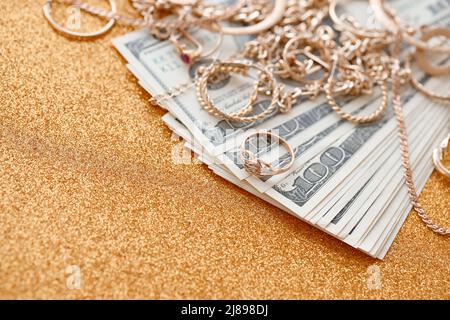 Many expensive golden jewerly rings, earrings and necklaces with big amount of US dollar bills on luxury glitter golden background surface. Pawnshop o Stock Photo