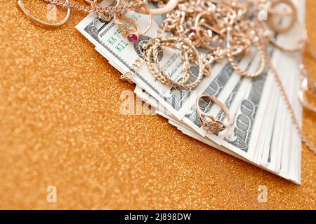 Many expensive golden jewerly rings, earrings and necklaces with big amount of US dollar bills on luxury glitter golden background surface. Pawnshop o Stock Photo