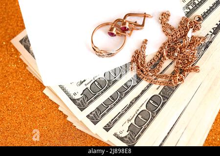 Expensive golden jewerly ring, earrings and necklace with big amount of US dollar bills on luxury glitter golden background surface. Pawnshop or jewer Stock Photo