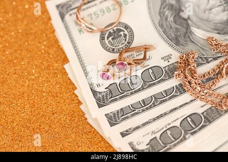 Expensive golden jewerly ring, earrings and necklace with big amount of US dollar bills on luxury glitter golden background surface. Pawnshop or jewer Stock Photo