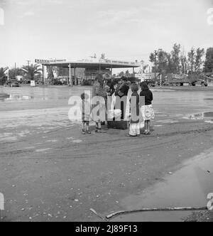 After a lift of five miles by a passing motorist, the family of homeless, walking people are left at the edge of the next town. [Signs: 'Mann's Super Service - 40 ft. Public Scales - Richfield Pennsylvania - Richlube Motor Oil']. Stock Photo