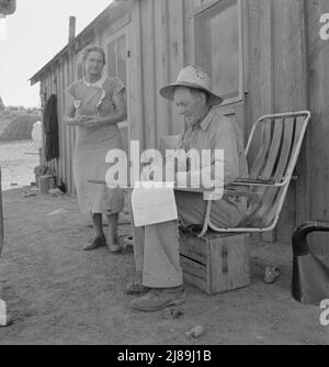 Oklahoma farmer, now living in Cow Hollow, is a FSA (Farm Security Administration) borrower. Seen here signing his chattel mortgage. Malheur County, Oregon. [Mr. and Mrs. Sam Cates. Note makeshift chair attached to wooden crate]. Stock Photo