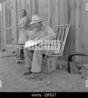 Oklahoma farmer, now living in Cow Hollow, is a FSA (Farm Security Administration) borrower. Seen here signing his chattel mortgage. Malheur County, Oregon. [[Mr. and Mrs. Sam Cates. Note makeshift chair attached to wooden crate]. Stock Photo