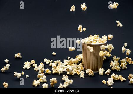 Popcorn is poured into a paper brown glass on a black background with place for text. Stock Photo