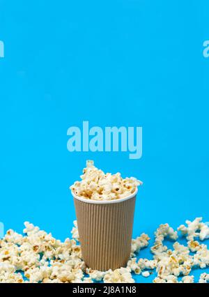 Popcorn in a glass and scattered on a blue background, a place for text. Stock Photo