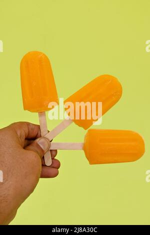 closeup the bunch orange color and flavor stick ice cream hold hand over out of focus brown background. Stock Photo