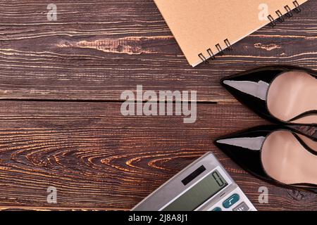 Shoes with calculator and notepad on brown wooden desk. Top view flat lay. Stock Photo