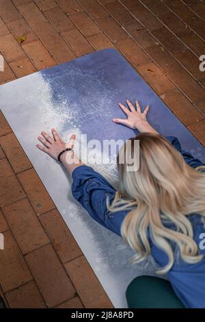 high angle shot from above of blonde caucasian spiritual lady in childs pose on her yoga mat focused on her long hair and widespread hands Stock Photo