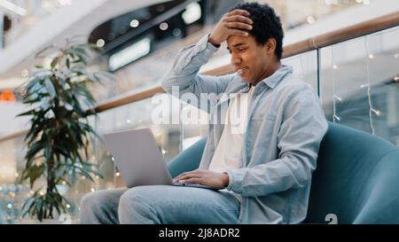 Multiracial guy freelancer african sad frustrated business man with laptop sitting on couch losing in online betting game lost money in internet Stock Photo