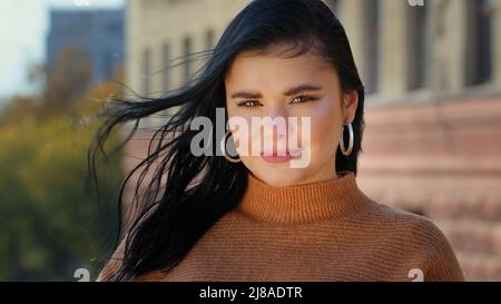Young attractive hispanic girl student model looking at camera posing standing alone outdoors for close-up portrait professional beautiful smiling Stock Photo