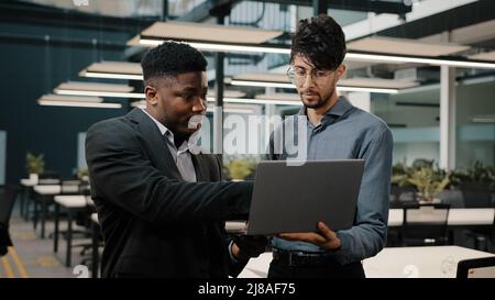 Two male business partners men Arabian man holding laptop showing presentation African businessman looking at computer screen colleagues working Stock Photo