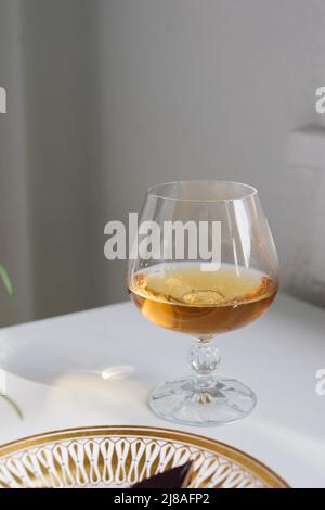 brandy snifter on white reflective table with white background by window Stock Photo