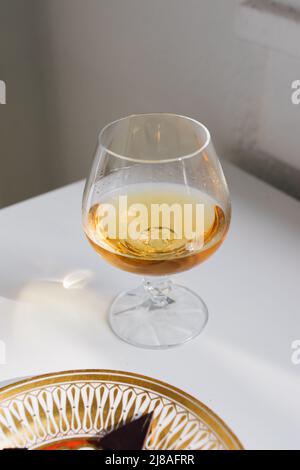 brandy snifter on white reflective table with white background by window Stock Photo